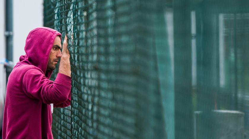 Refugiado olha através da rede no centro de acolhimento de refugiados em Mecklenburg-Western Pomerania, Horst, Alemanha. Foto: EPA/JENS BUETTNER